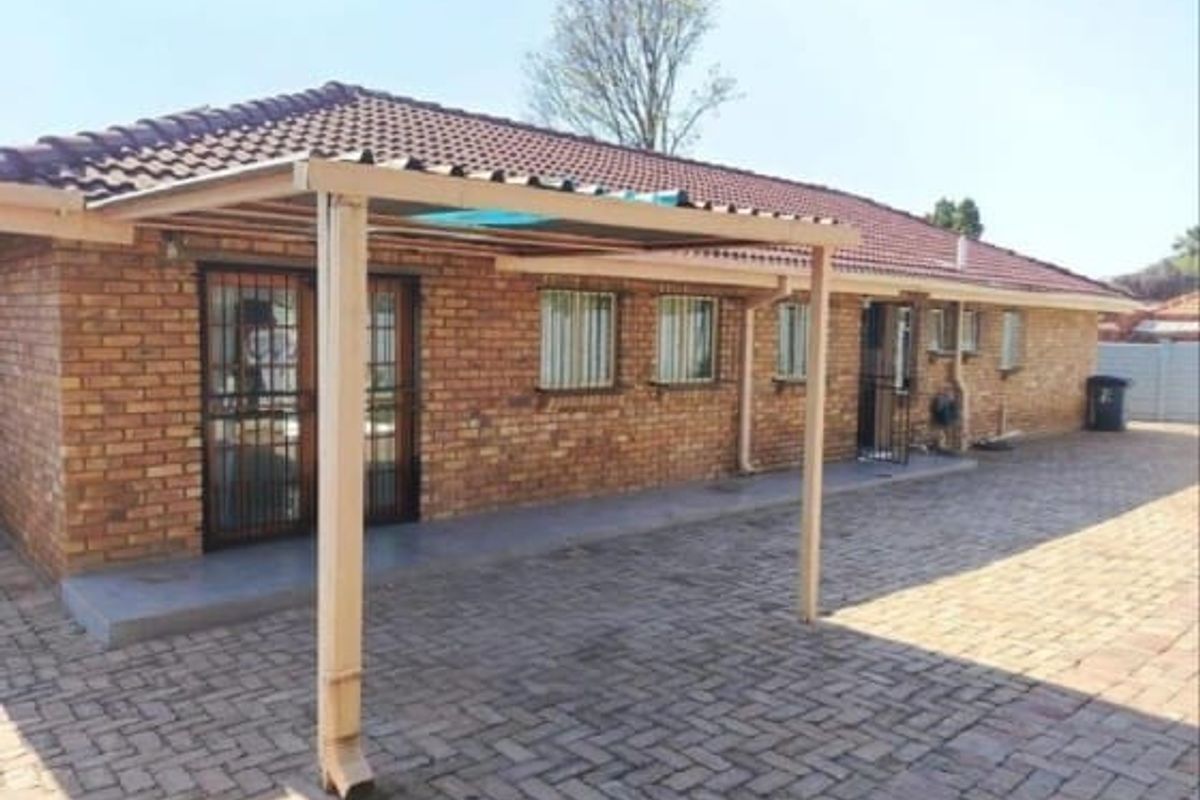Rear view of the house featuring a brick facade, tiled roof, and a covered patio area with paved surroundings.