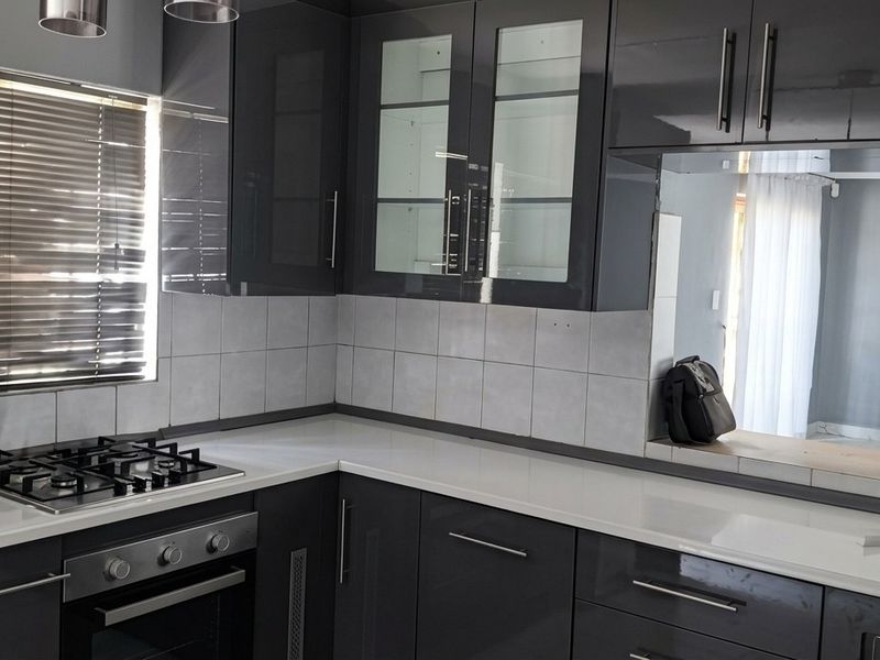Modern kitchen featuring high-gloss dark cabinetry, stone countertops, a gas hob, and a built-in oven with a clean tiled backsplash.