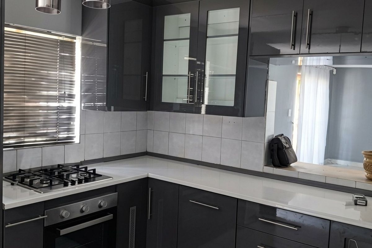 Modern kitchen featuring high-gloss dark cabinetry, stone countertops, a gas hob, and a built-in oven with a clean tiled backsplash.