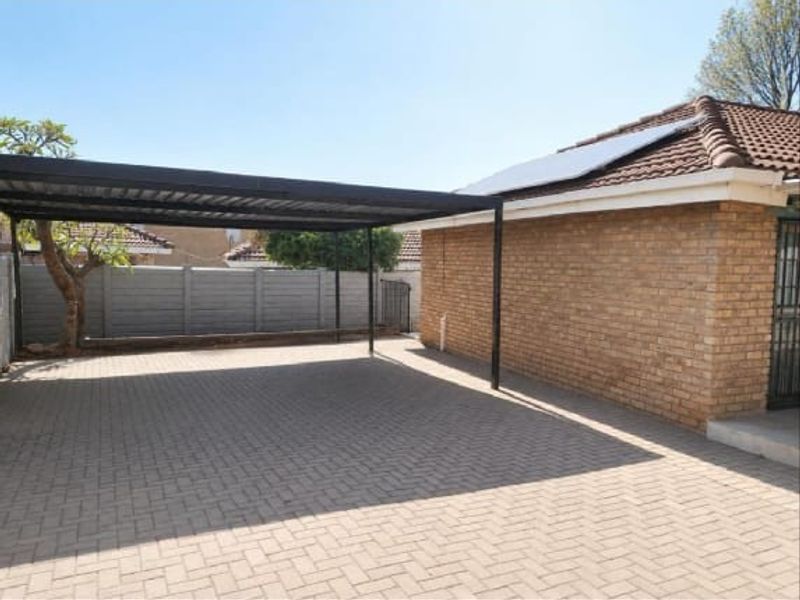 A paved rear exterior area featuring a covered carport, brick wall construction, and solar panels installed on the tiled roof.
