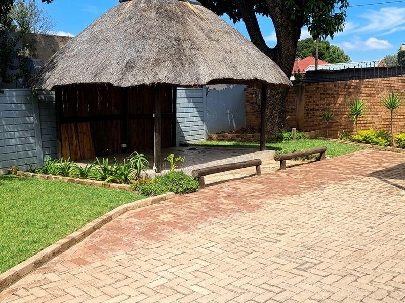 Outdoor entertainment area featuring a traditional thatch lapa, paved patio space, and established garden boundaries, ideal for renovation and landscaping potential.