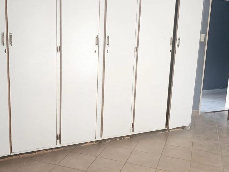 A bedroom featuring built-in white cupboards and tiled flooring, currently vacant and ready for updates.
