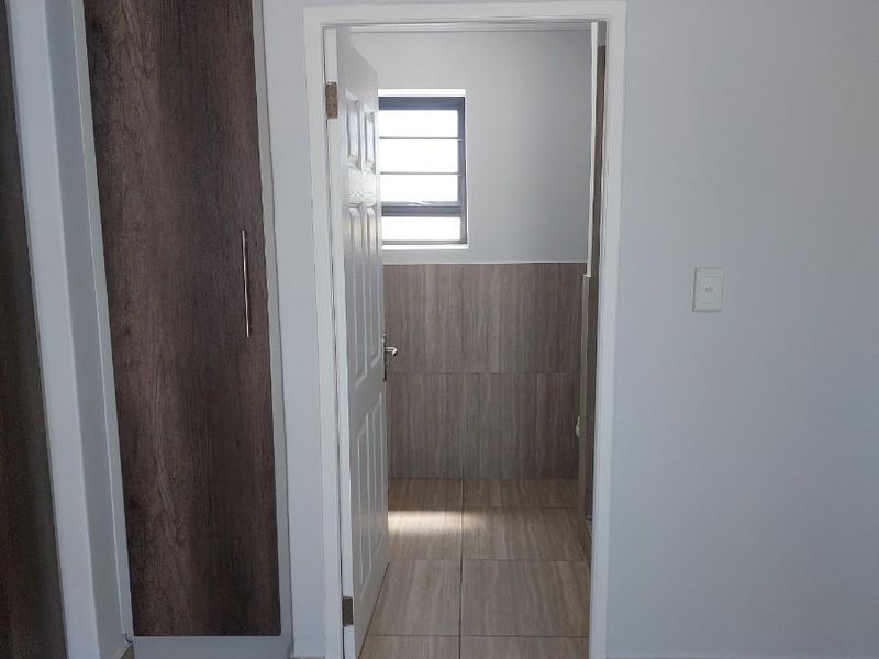 A clean, empty bedroom featuring modern wood-look tiled flooring and built-in cupboards, with an open doorway leading to an adjacent tiled bathroom.