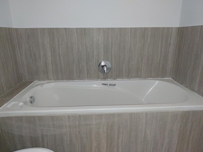A clean bathroom featuring a built-in bathtub with neutral wood-look wall tiling and a modern chrome mixer tap.