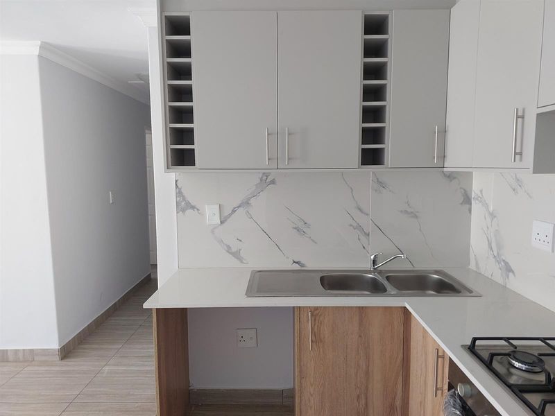 Modern kitchen featuring light wood-tone cabinetry, marble-look splashback, stone countertops, and a built-in gas hob with a double bowl stainless steel sink.