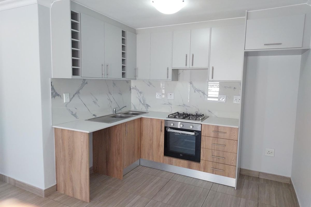 Modern kitchen featuring light wood-tone lower cabinets, white upper cabinetry, marble-look splashback, gas hob, and built-in oven.