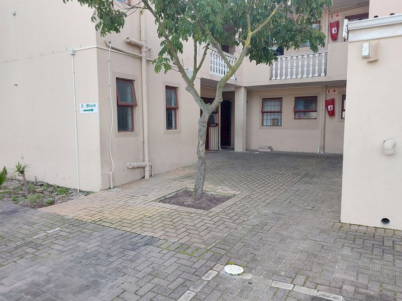 Exterior view of the apartment complex entrance featuring paved driveway, building facade with balustrades, and directional signage.