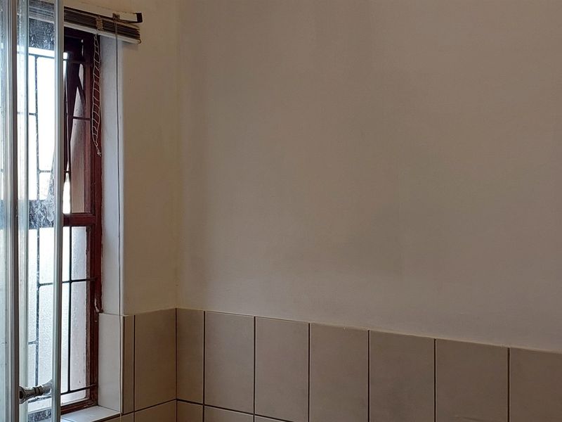 A view of a bathroom corner featuring tiled splashbacks and a window with security bars, showing signs of wear and requiring maintenance.