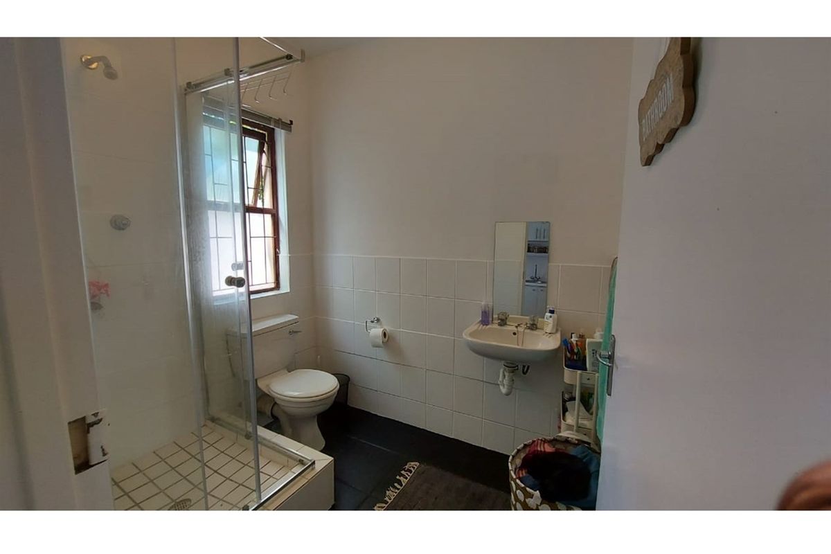 A functional bathroom featuring a shower enclosure, wall-mounted basin, and toilet, with tiled splashbacks and a window providing natural light.