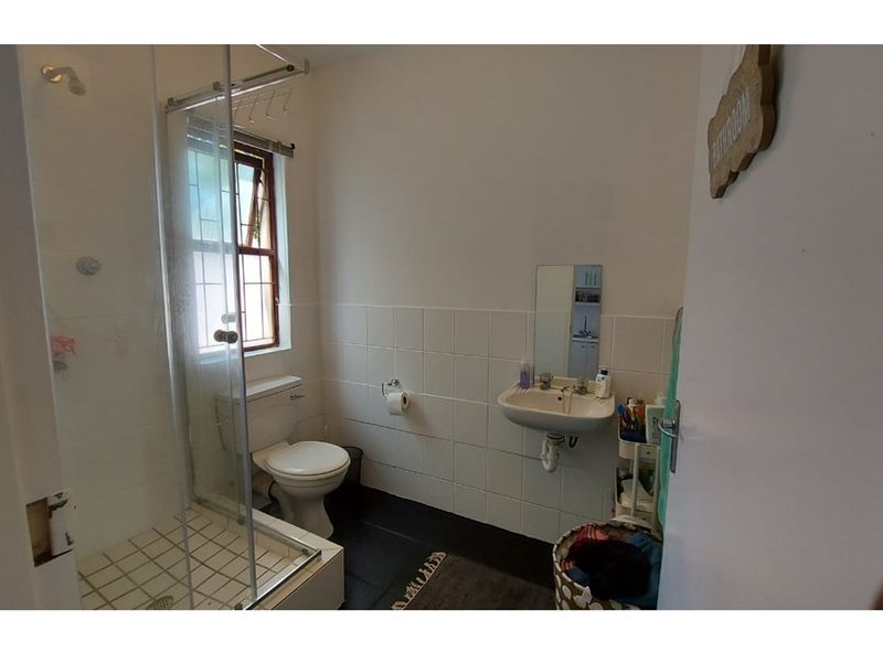 A functional bathroom featuring a shower enclosure, wall-mounted basin, and toilet, with tiled splashbacks and a window providing natural light.