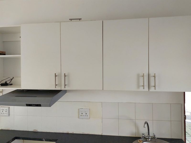 A functional kitchen area featuring white built-in cabinetry, a tiled backsplash, an extractor fan, and a stainless steel sink with a faucet.