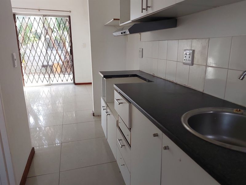 A compact kitchen featuring built-in cabinetry, a stainless steel sink, and tiled flooring, leading directly to an outdoor area through a sliding glass door.