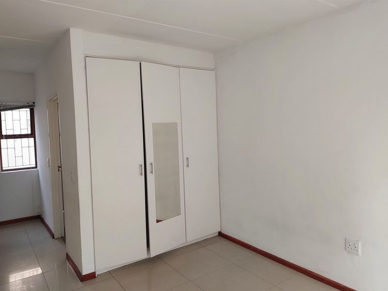 A clean, empty bedroom featuring neutral tiled flooring and white built-in cupboards with a central mirror panel.