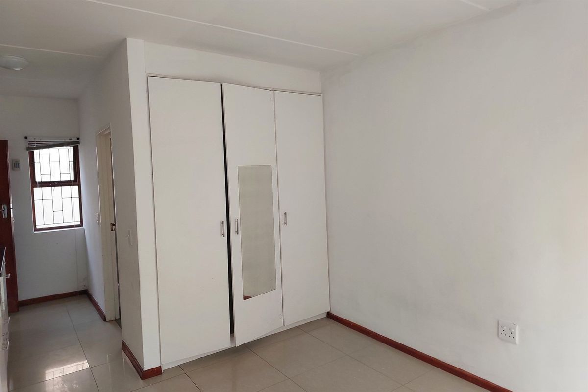A clean, empty bedroom featuring neutral tiled flooring and white built-in cupboards with a central mirror panel.