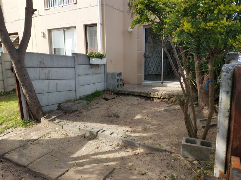 Rear exterior view of the apartment featuring a small paved patio area and a private garden space enclosed by a precast concrete wall.