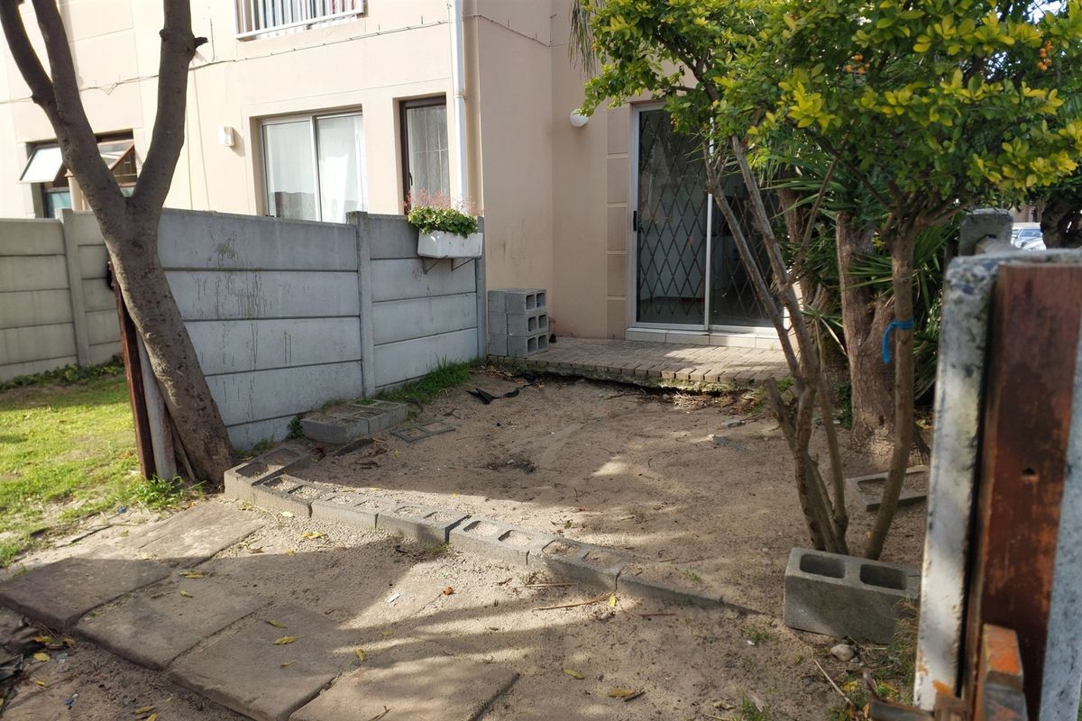 Rear exterior view of the apartment featuring a small paved patio area and a private garden space enclosed by a precast concrete wall.