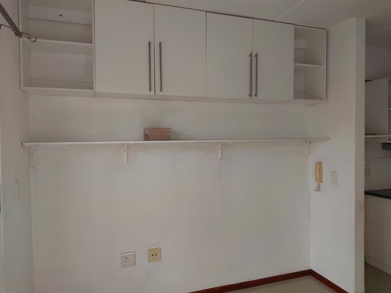 A functional kitchen area featuring white built-in wall cabinetry, open shelving, and tiled flooring, providing a clean and neutral space for culinary activities.