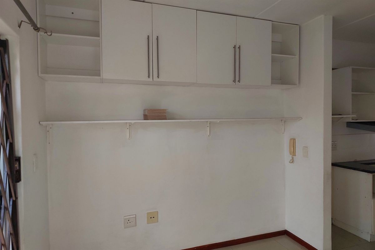 A functional kitchen area featuring white built-in wall cabinetry, open shelving, and tiled flooring, providing a clean and neutral space for culinary activities.