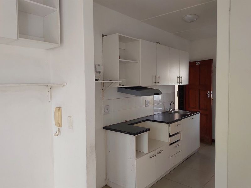A compact kitchen area featuring white built-in cabinetry, a dark laminate countertop, a stainless steel sink, and an extractor fan.