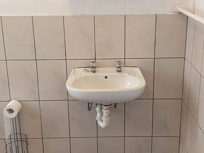 A functional bathroom space featuring a wall-mounted ceramic basin with chrome taps and neutral wall tiling.