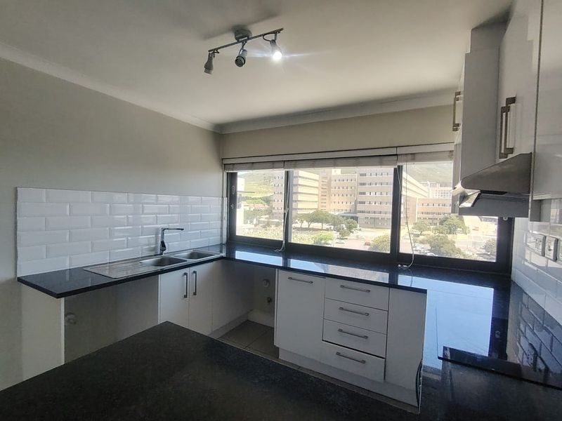 A clean, modern kitchen featuring granite countertops, white cabinetry, subway tile backsplash, and a large window with an urban view.
