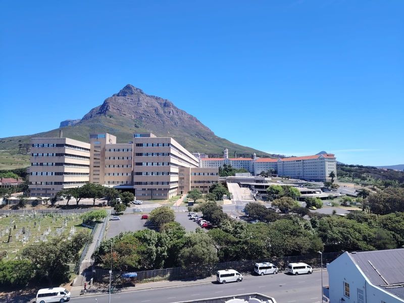 A wide-angle view of a large institutional building complex set against a prominent mountain backdrop under a clear blue sky.