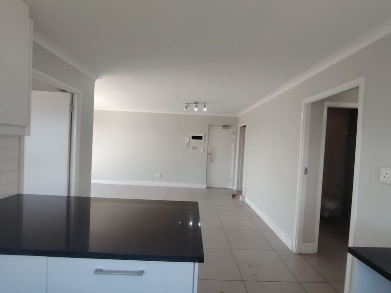 Spacious open-plan living area featuring neutral tiled flooring, modern granite kitchen countertops, and clean finishes, providing a versatile layout for contemporary apartment living.