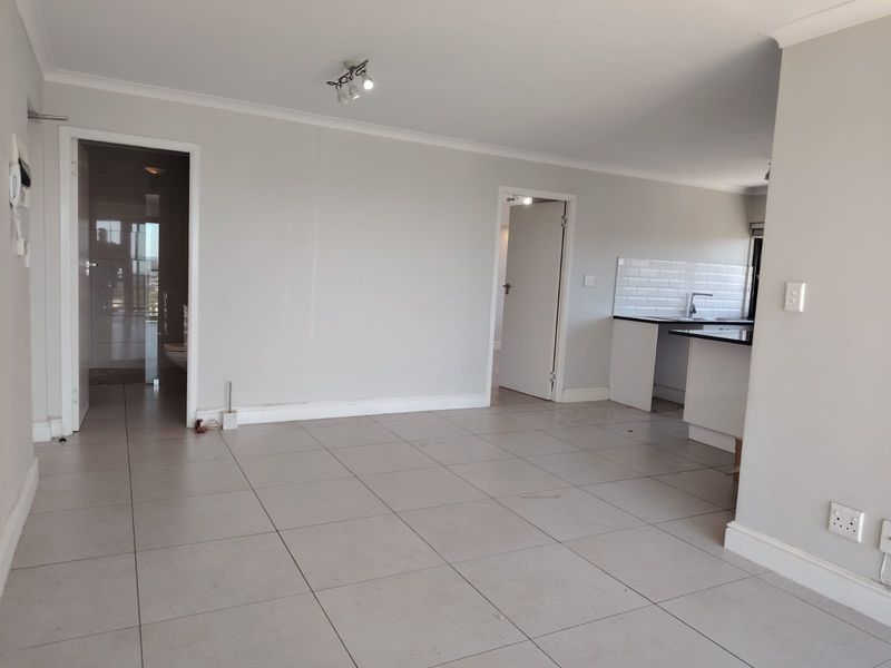 An open-plan living area featuring neutral tiled flooring, a modern kitchen with subway tile backsplash, and direct access to adjacent rooms.