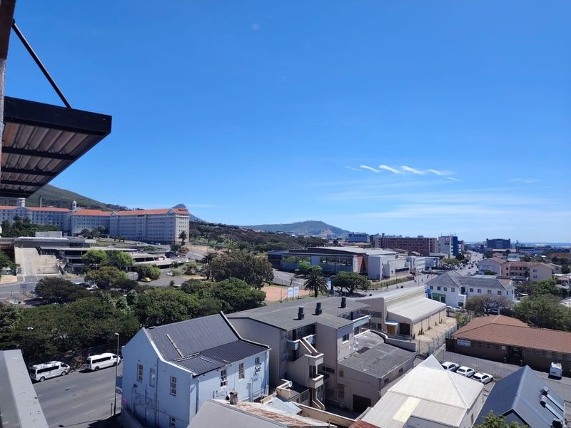 An elevated urban view overlooking the surrounding neighborhood, nearby commercial buildings, and distant mountain landscape under a clear blue sky.
