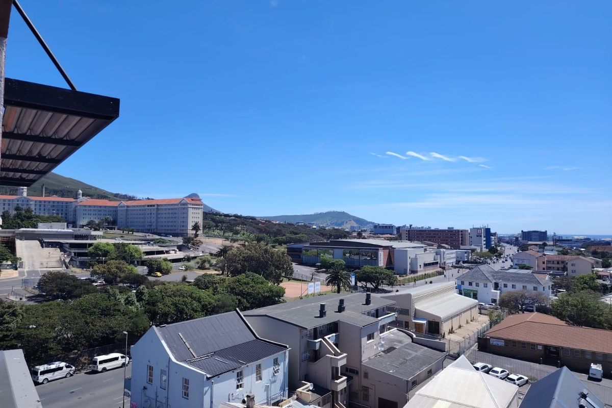 An elevated urban view overlooking the surrounding neighborhood, nearby commercial buildings, and distant mountain landscape under a clear blue sky.