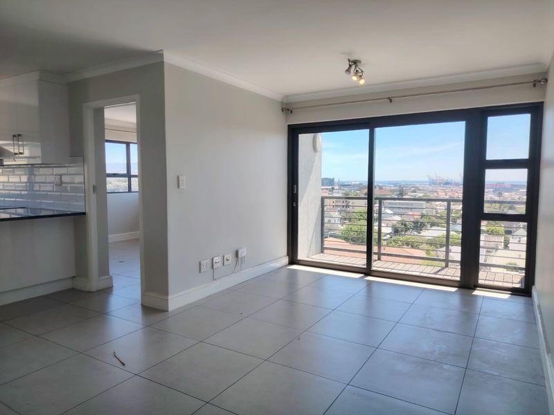 Bright open-plan living area featuring neutral tiled floors, modern kitchen cabinetry, and large sliding doors opening to a balcony with expansive city views.
