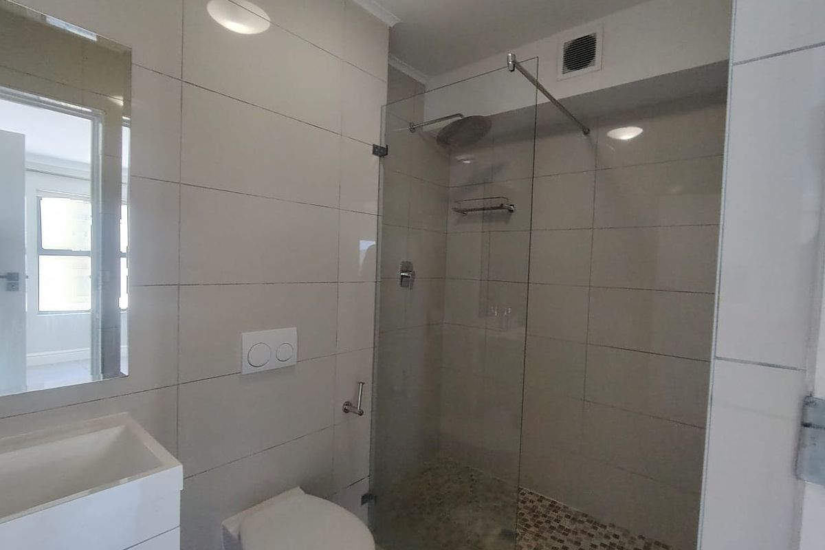 Modern bathroom featuring a walk-in shower with glass screen, wall-mounted toilet, and a vanity basin with neutral wall tiling.