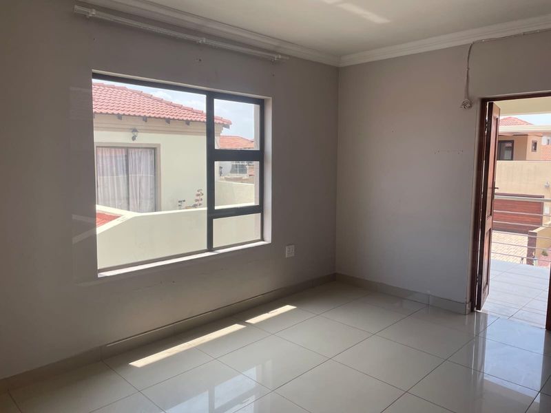 An empty bedroom featuring tiled flooring, neutral walls, and an aluminium window frame, offering a blank canvas for interior design.