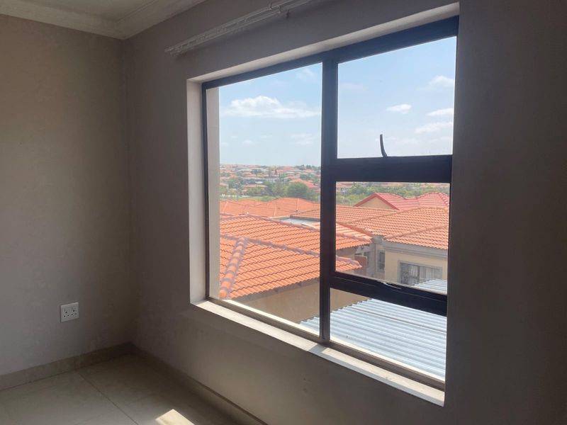 An empty bedroom featuring tiled flooring and a large aluminium window with views over the surrounding neighbourhood.