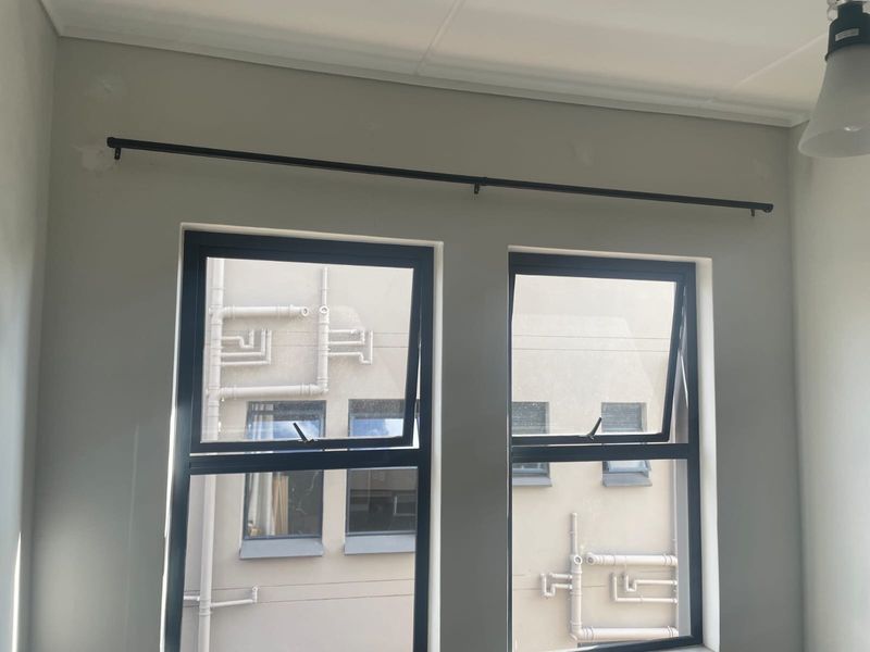 A bright, empty bedroom featuring modern dark aluminium window frames and a fitted curtain rod, ready for personal styling.