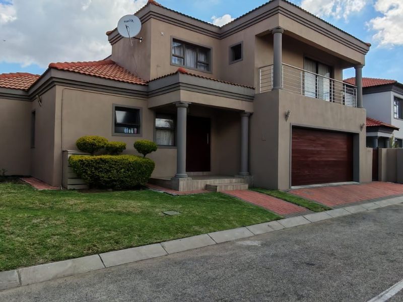 A well-maintained double-story residential house featuring a tiled roof, integrated double garage, and an upper-level balcony with a paved driveway and front garden.