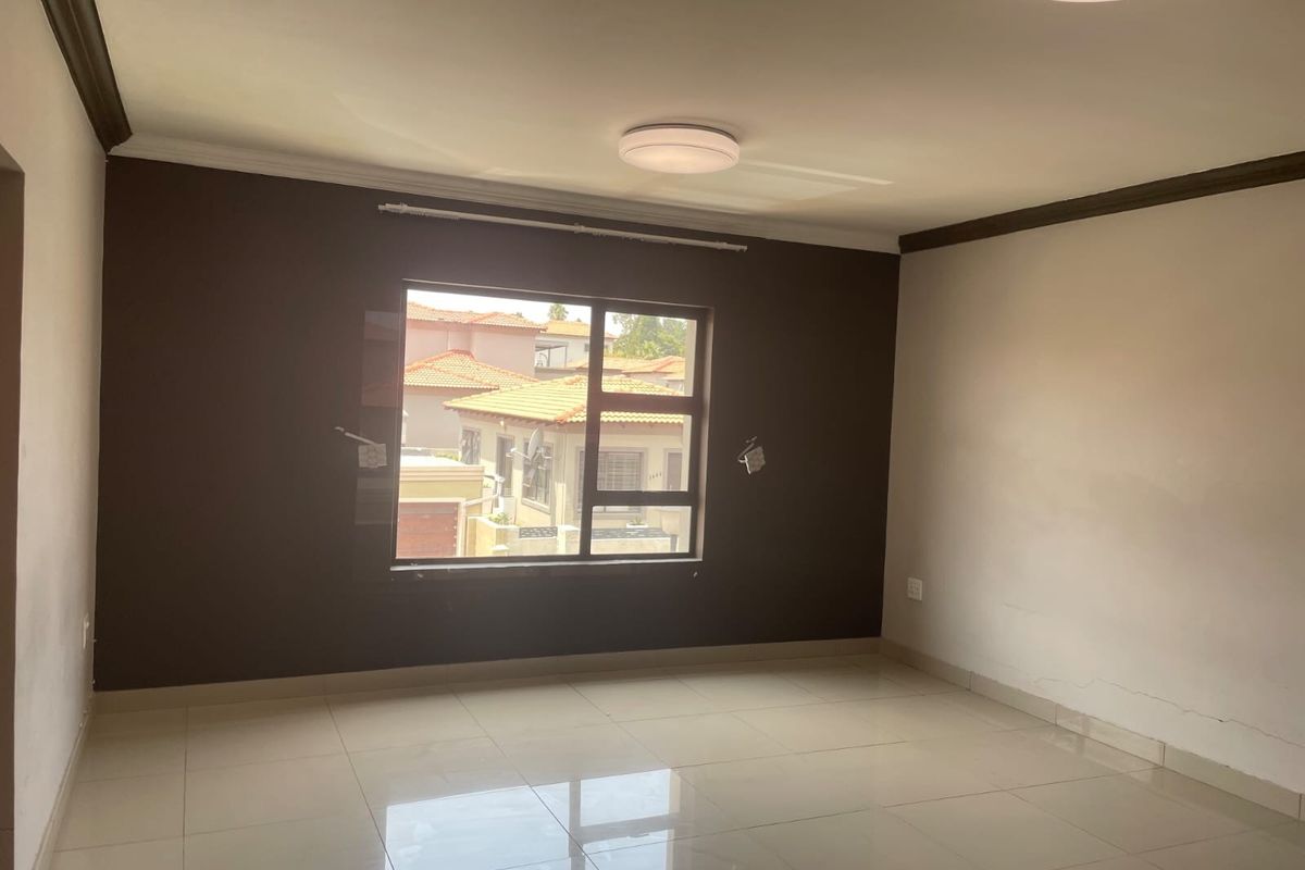 An empty living room featuring tiled flooring, neutral wall tones, and a large window providing natural light and a view of the surrounding residential area.