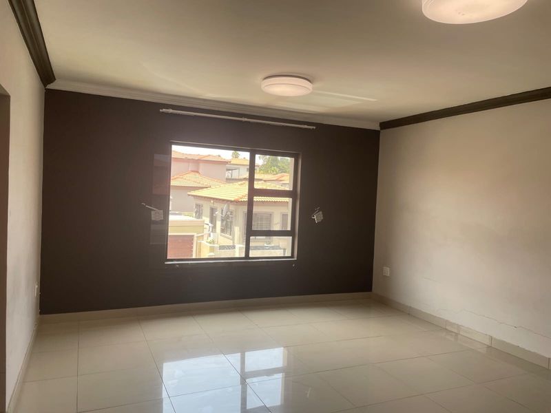 An empty living room featuring tiled flooring, neutral wall tones, and a large window providing natural light and a view of the surrounding residential area.