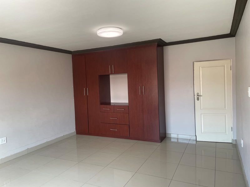 A spacious, empty bedroom featuring neutral tiled flooring, dark wood built-in cupboards, and a classic panel door.