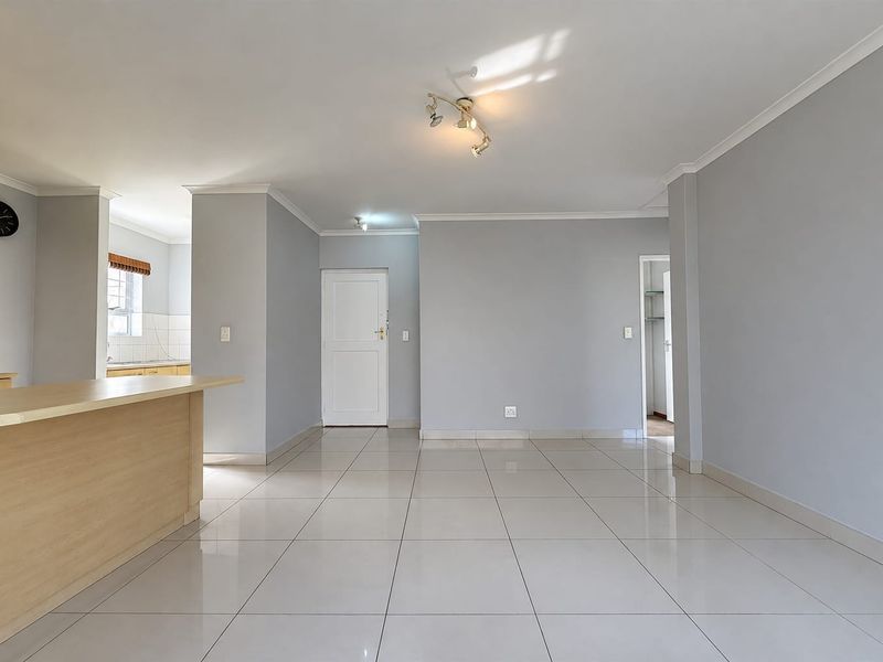 Spacious open-plan living area featuring neutral tiled flooring, a breakfast counter, and clean finishes, providing a versatile space for dining and relaxation.