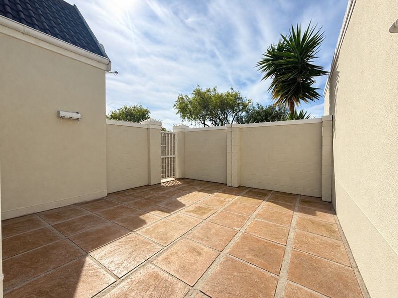 A private, paved outdoor patio area enclosed by high boundary walls with a secure metal gate, offering a low-maintenance space for outdoor living.