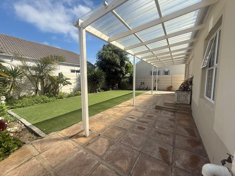 A spacious outdoor patio featuring a covered pergola, paved flooring, and a well-maintained artificial lawn area, perfect for outdoor relaxation and entertaining.