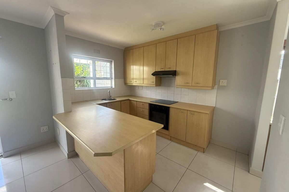 A functional kitchen featuring light wood cabinetry, a breakfast bar, built-in oven and hob, and tiled flooring throughout.