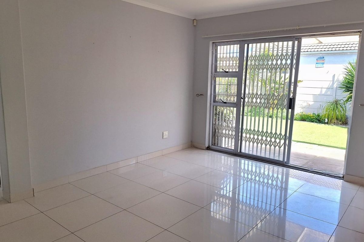 An empty living room featuring polished floor tiles and a sliding glass door with a security gate, providing direct access to the rear garden.