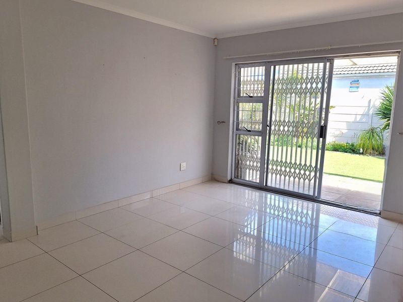 An empty living room featuring polished floor tiles and a sliding glass door with a security gate, providing direct access to the rear garden.