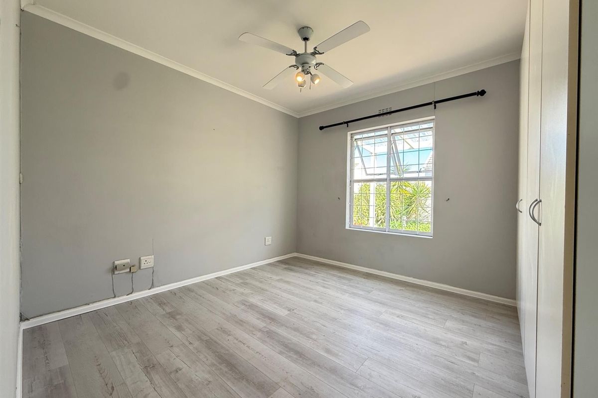 A bright, empty bedroom featuring light-toned laminate flooring, built-in cupboards, and a ceiling fan, providing a clean canvas for personalization.