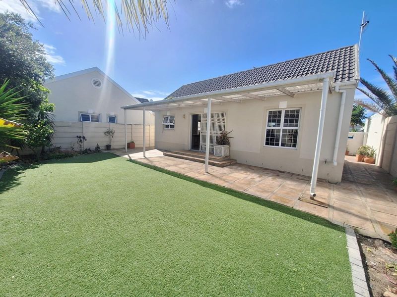 Rear view of the property featuring a paved patio area with a covered pergola, artificial lawn, and secure boundary walls.