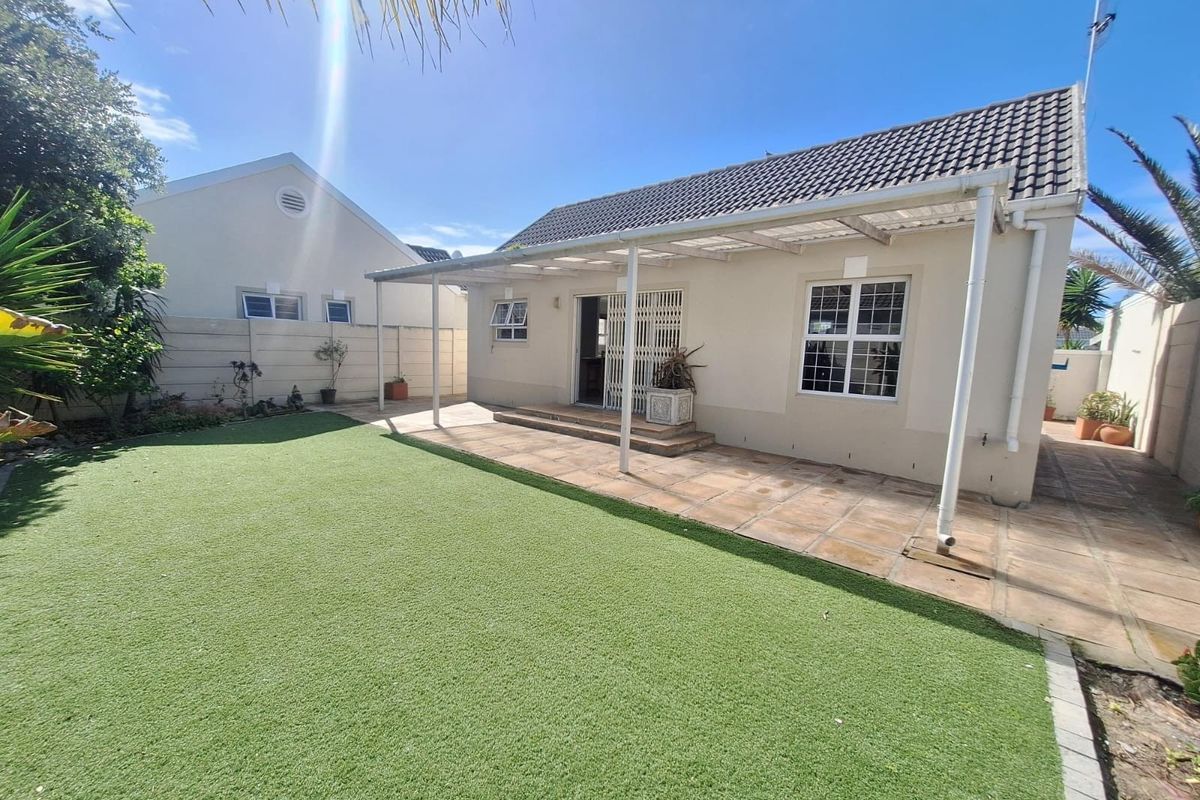 Rear view of the property featuring a paved patio area with a covered pergola, artificial lawn, and secure boundary walls.