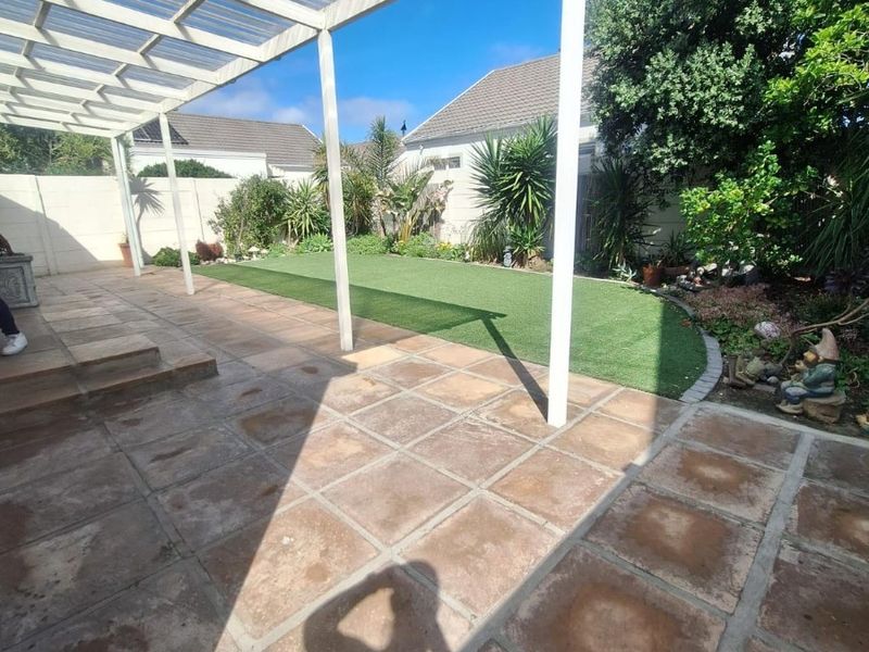 A covered outdoor patio area featuring paved flooring and an adjacent artificial lawn, providing a functional space for outdoor living and entertainment.