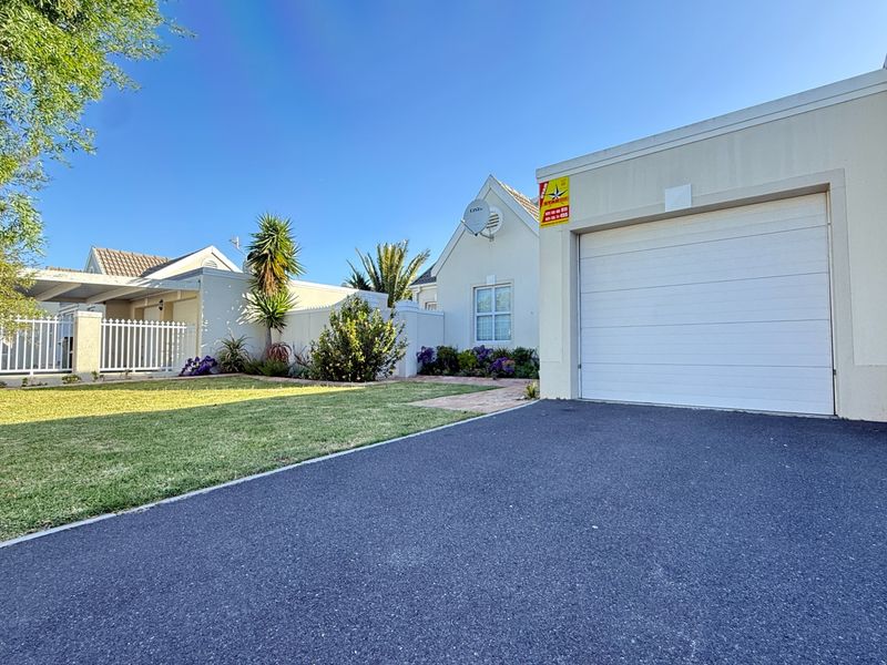 Front view of the property featuring a paved driveway, single garage, and a well-maintained front garden with a white picket fence.